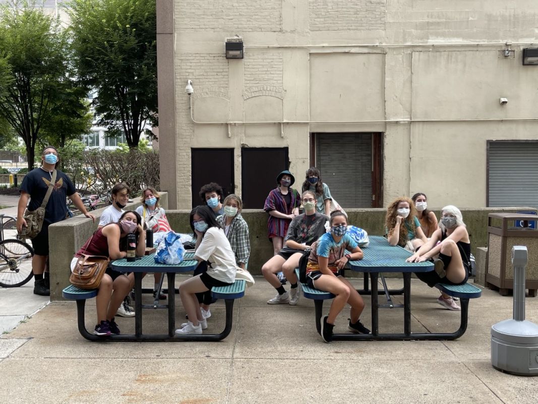 students sitting at outdoor tables in front of residence hall with face masks