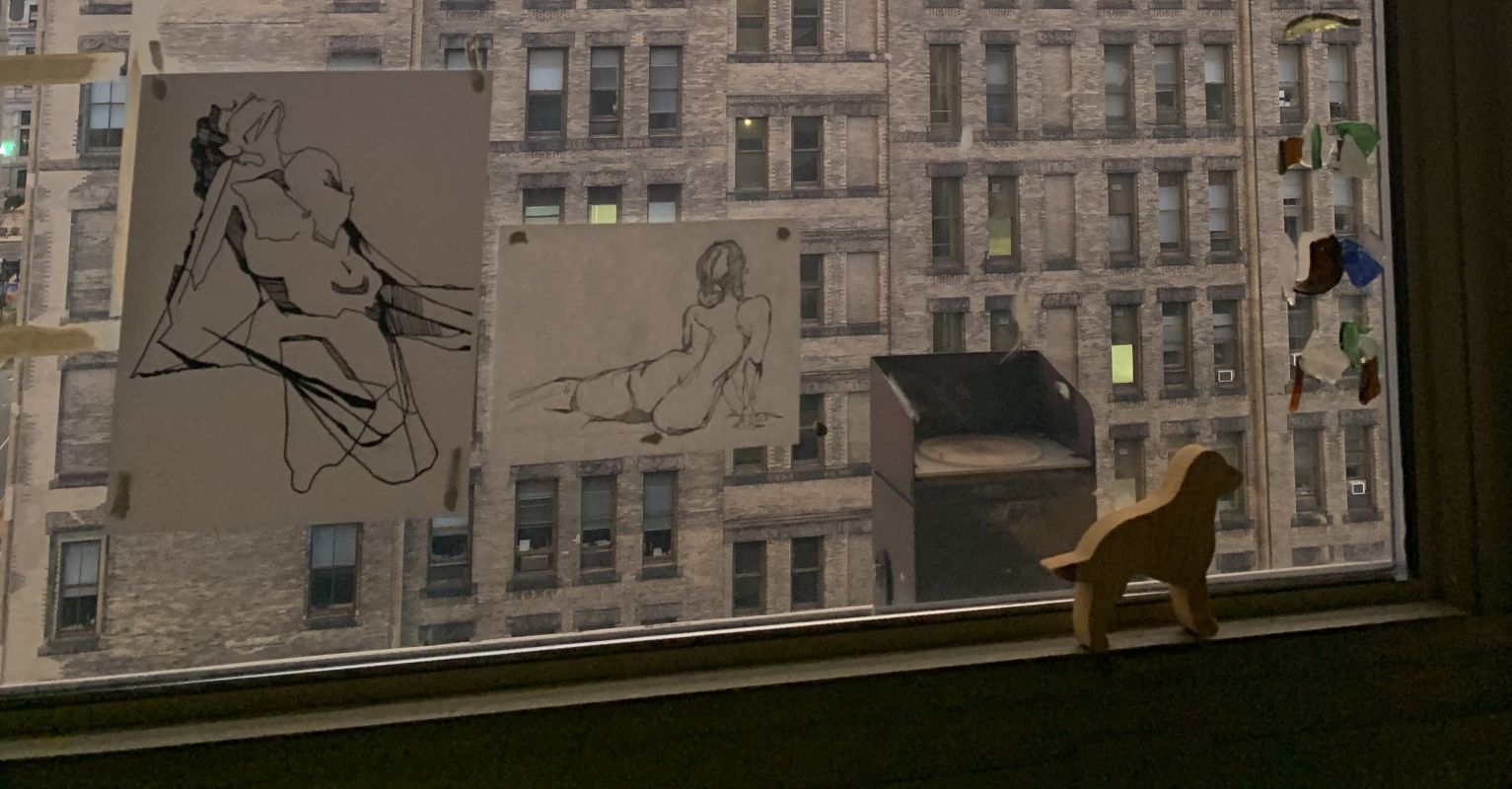 ink drawings of nude figures taped to window with large building in the background
