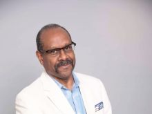 Bio photo of Allan L. Edmunds a brown-skinned man with a mustache. He is wearing glasses and a white suite jacket with a light blue button-down shirt. 