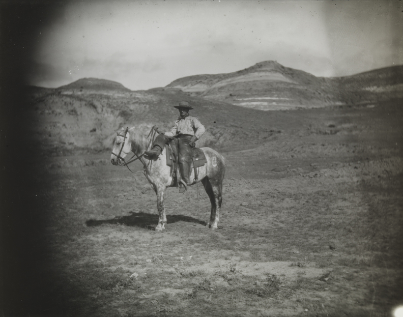 Cowboy in buckskin shirt, on dappled horse, right leg over pommel