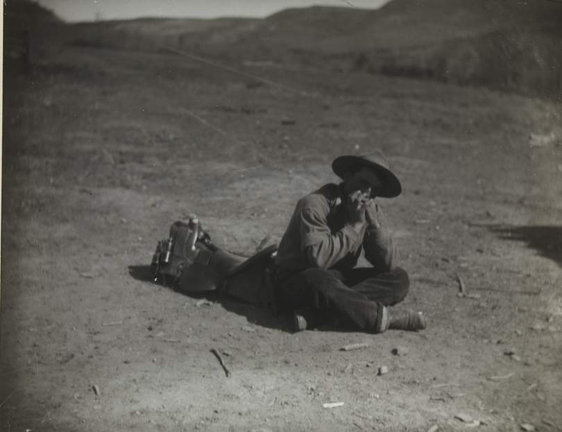 Cowboy sitting on ground playing harmonica
