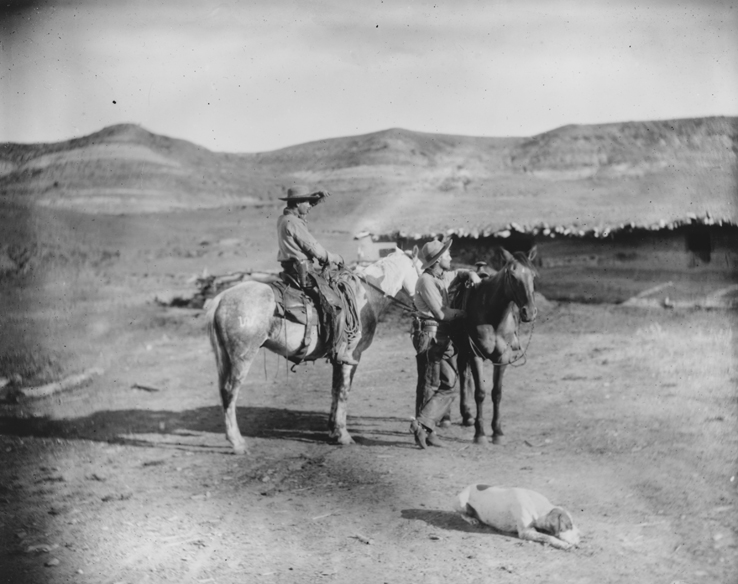 Two cowboys, with horses in BT Ranch yard, dog in foreground