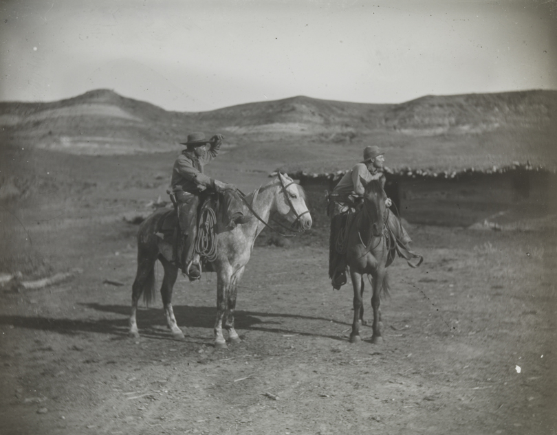 Two cowboys on horses in BT Ranch yard, cowboy at left shielding eyes