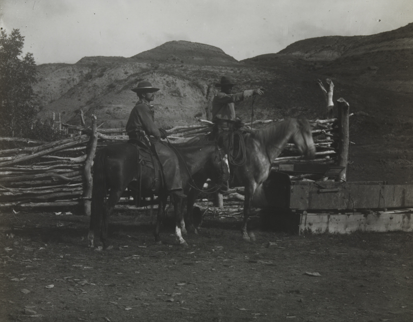 Two cowboys on horses in front of corral at BT Ranch