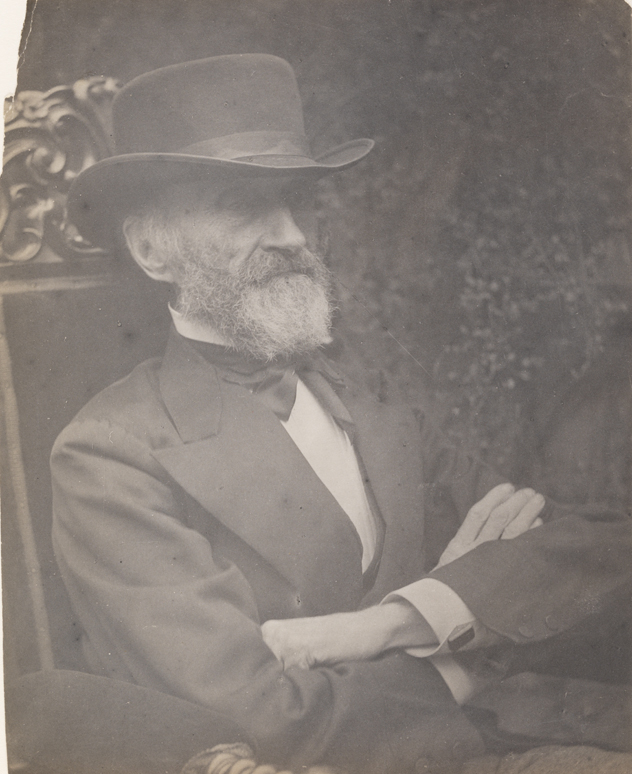 George W. Holmes facing right, sitting, arms folded, in carved armchair