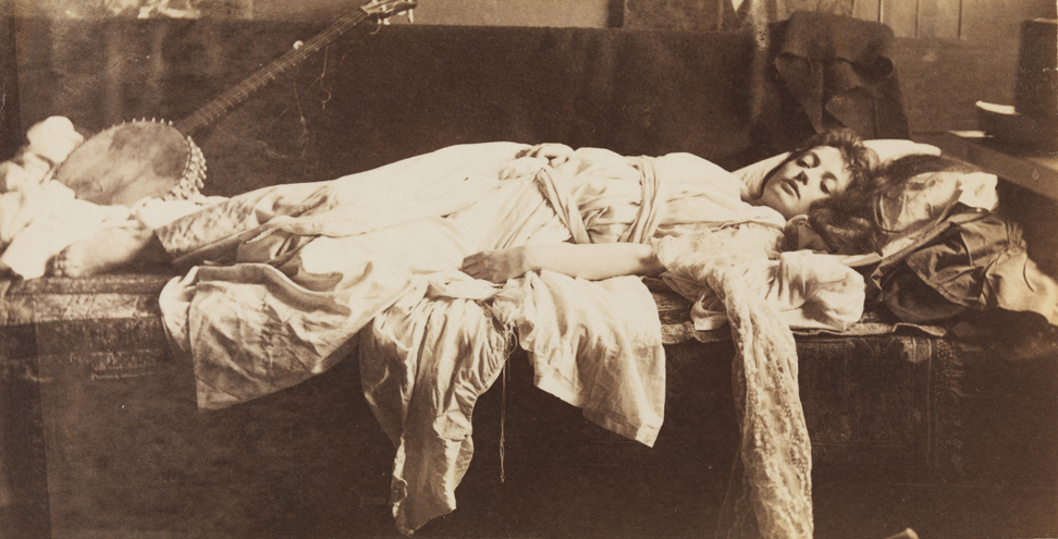 Blanche Gilroy in classical costume, reclining, with banjo