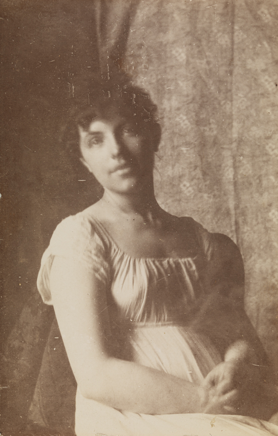 Woman in Empire dress, sitting in front of printed-fabric backdrop