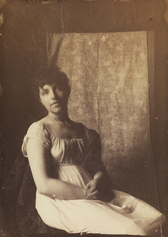 Woman in Empire dress, sitting in front of printed-fabric backdrop