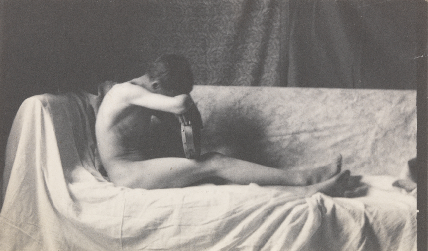 Male nude on draped couch, forearm and head resting on tambourine