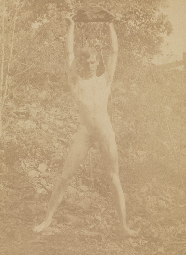Male nude, holding large rock above head, in wooded landscape