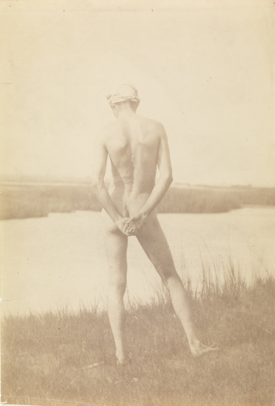 Male nude wearing head scarf, from rear, at edge of river