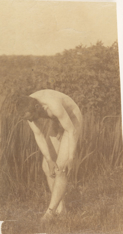 Thomas Eakins nude, bending forward, hands grasping left knee, in tall grass