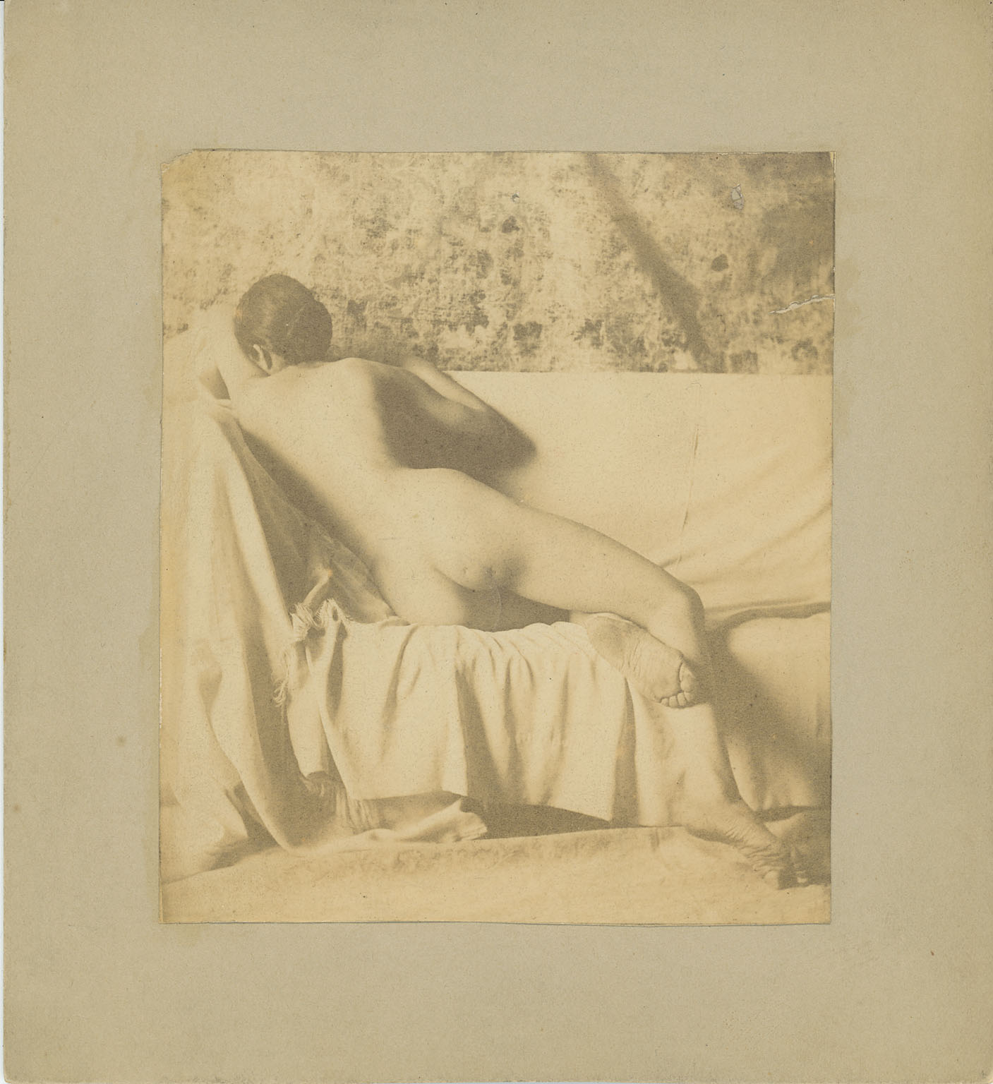 Female nude semireclining, on draped couch, from rear