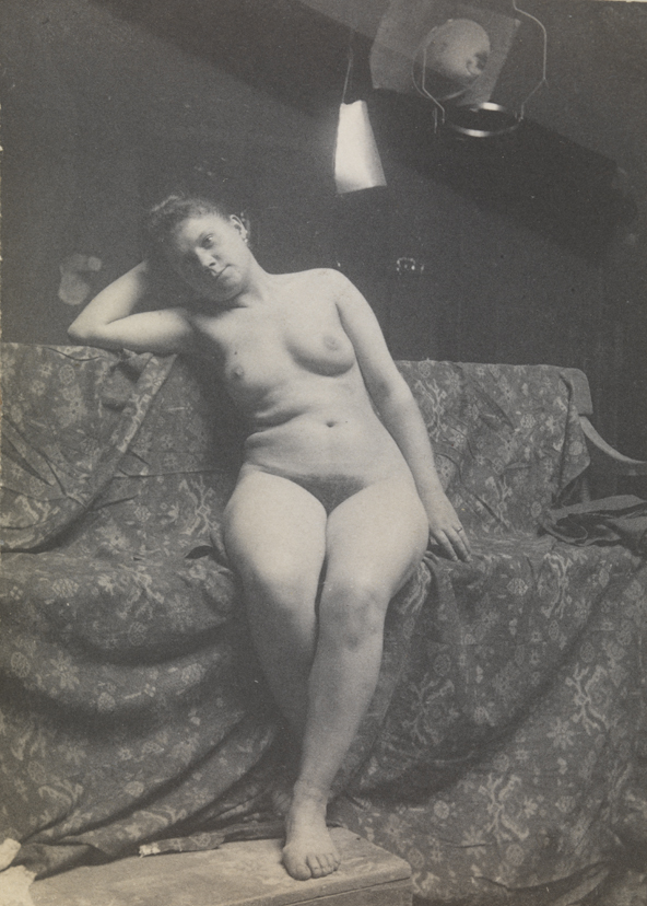 Female nude sitting on draped couch, foot on stool