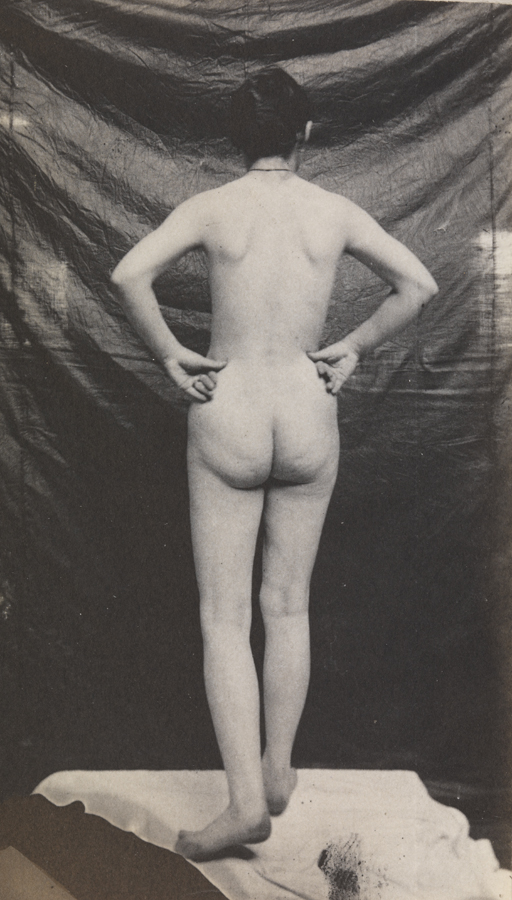 Female nude standing on cloth, hands on hips, from rear