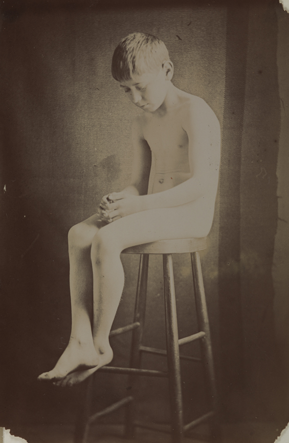 Boy nude, sitting on stool, in studio