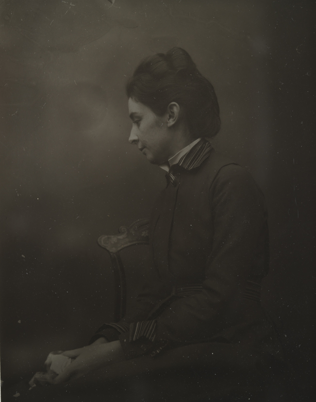 Unidentified woman sitting, facing left, in chair with painted crest                     