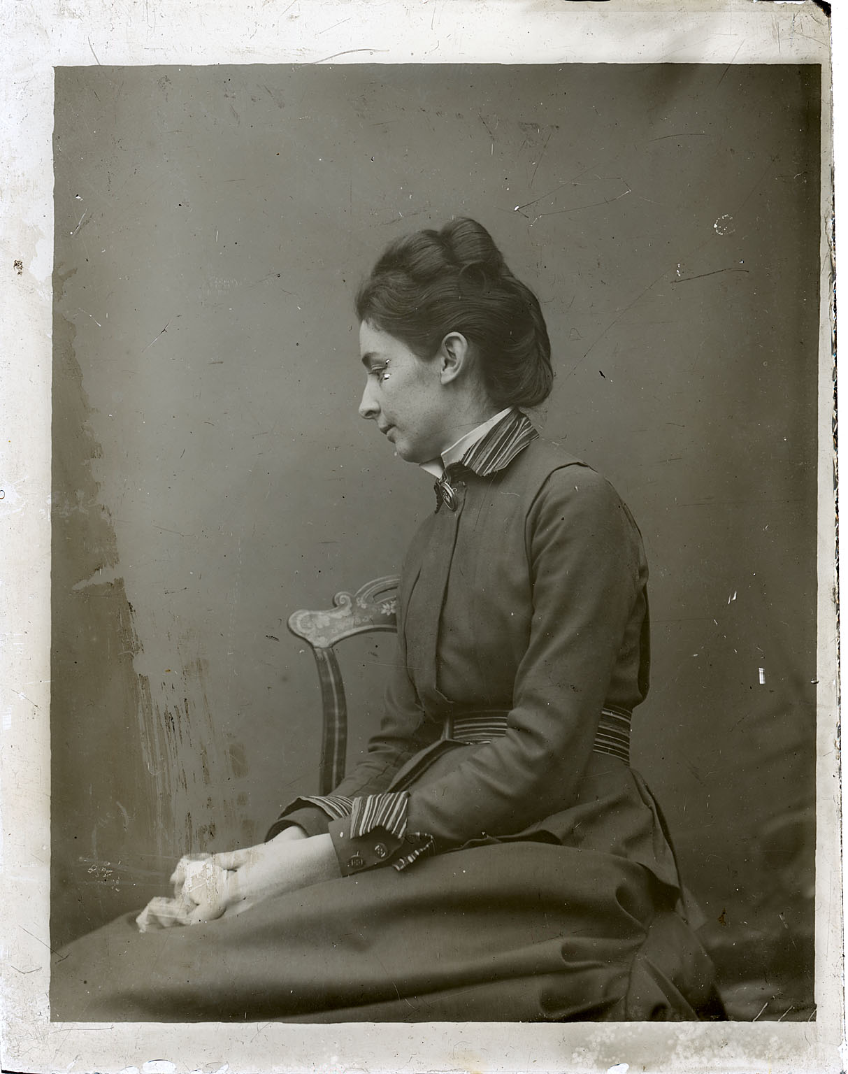 Unidentified woman sitting, facing left, in chair with painted crest                     