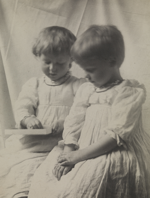 Two children in light dresses, one holding box