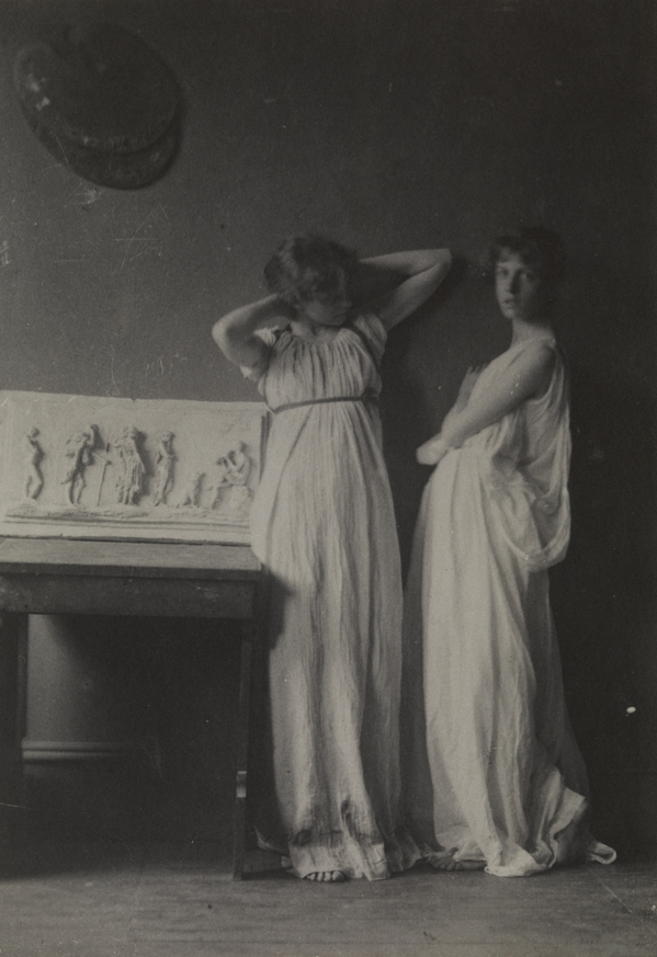 Two women in classical costume, with Thomas Eakin's "Arcadia" relief at left