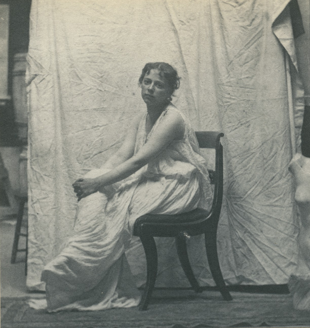 Weda Cook in classical costume, sitting in Empire chair