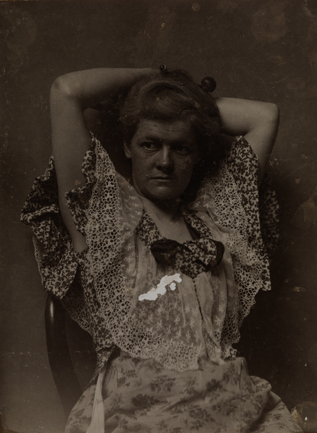 Elizabeth Macdowell in print dress, sitting, hands behind head