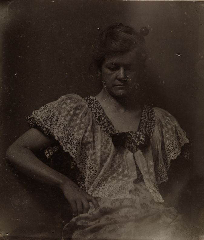 Elizabeth Macdowell in print dress, sitting, looking down