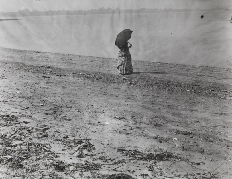 Woman in plaid dress with parasol at edge of Delaware River     