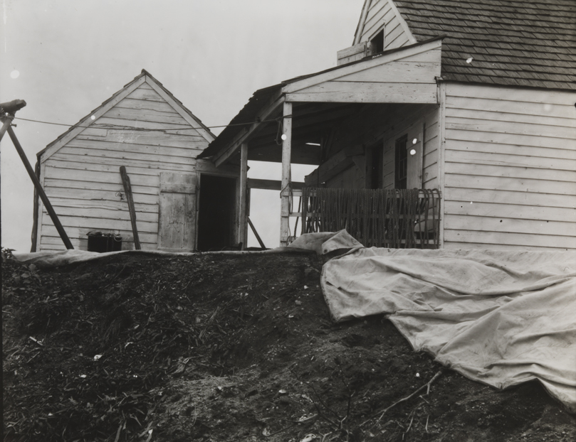 Clapboard house with ropes on porch and sail on ground          