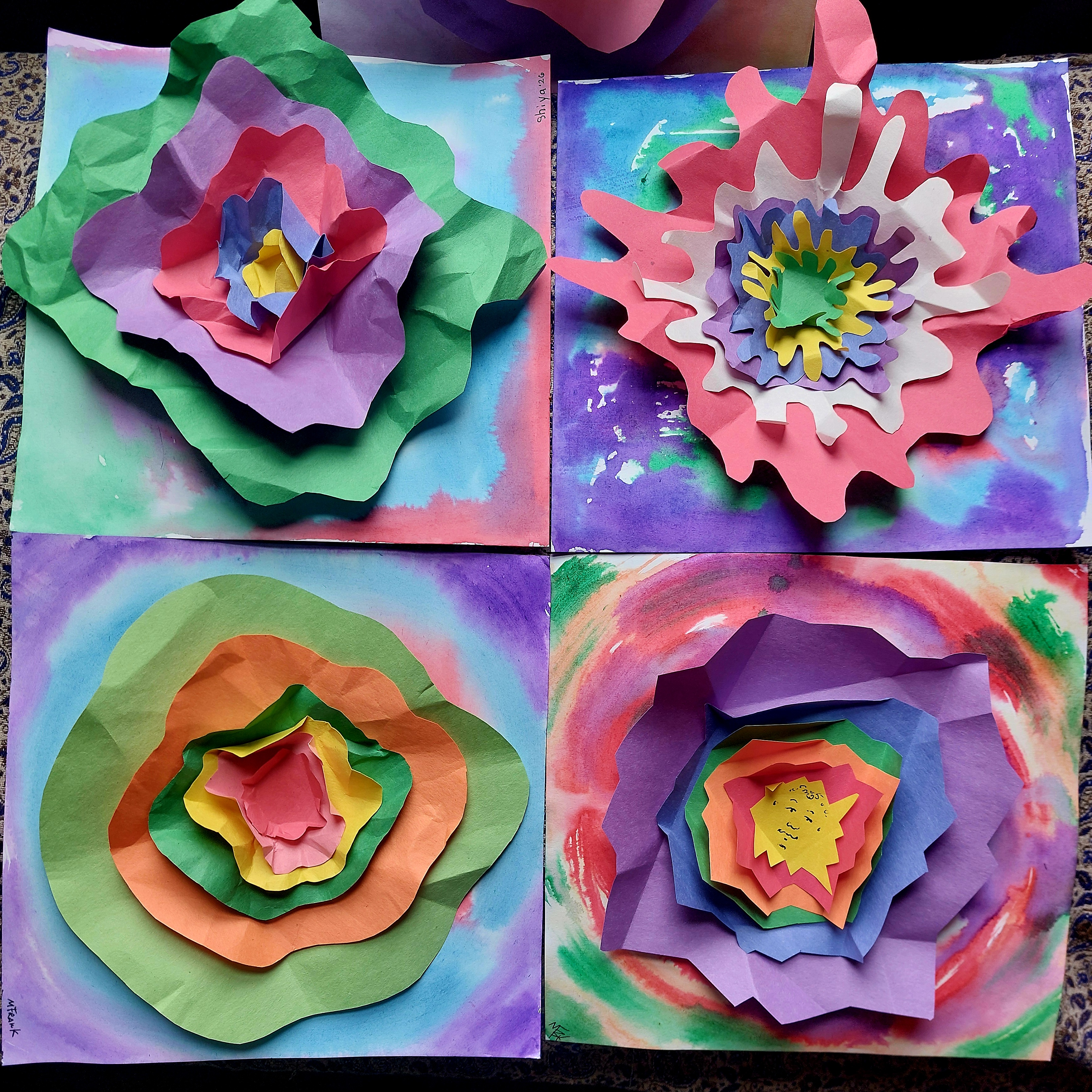 Colorful paper flowers are crafted from layered petals in green, purple, pink, and orange on a vibrant, watercolor background, evoking a joyful ambiance.