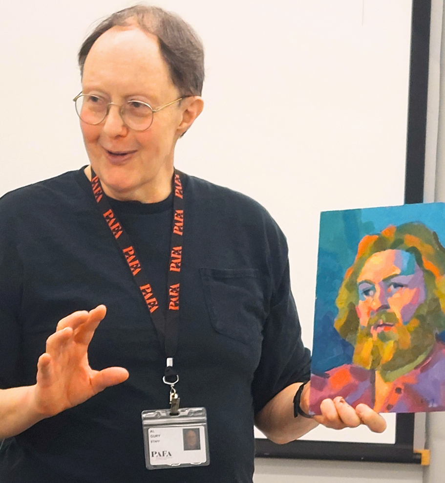 A man with round glasses wearing a PAFA lanyard gestures with his right hand while holding up a vibrant, multicolored painted portrait of a bearded man in his left hand.