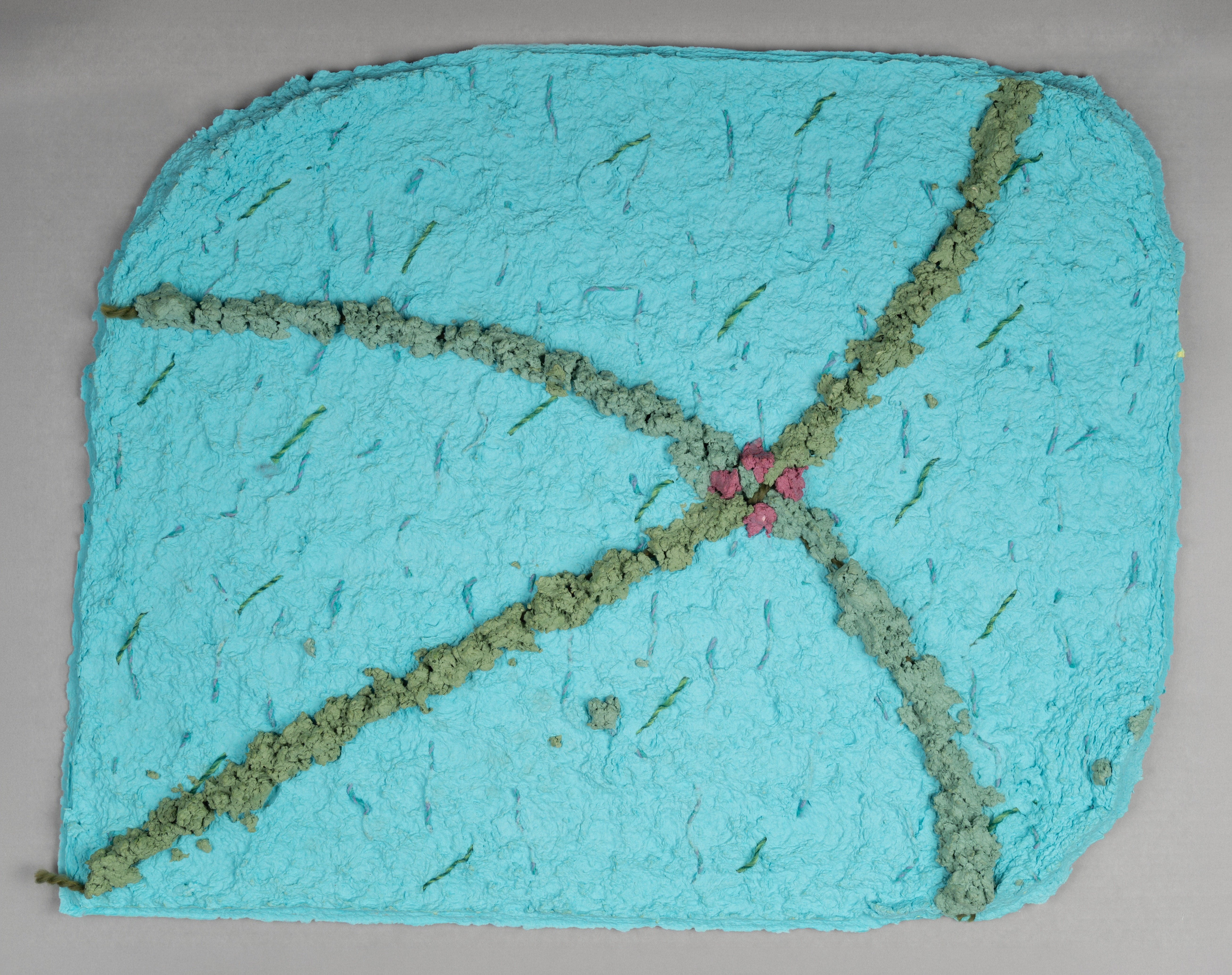 A textured turquoise handmade paper artwork features intersecting grayish-green fibrous lines that meet at a central cluster of small pink floral shapes.