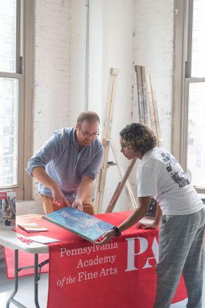 two people looking at painting over table with red tablecloth with pafa logo