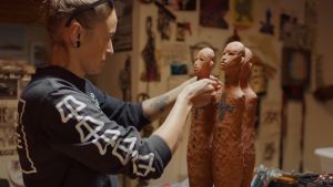 Artist in her studio working on three clay figures, each about 16 inches tall. 