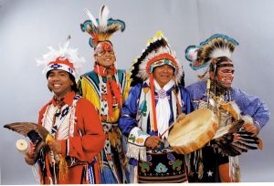 Studio portrait of four members of Thunderbird American Indian Dancers dressed in full regalia for performance