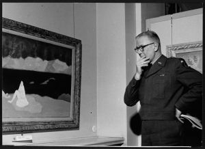 black and white photo of Gen. Lemuel Mathewson on left side of the frame, his left hand pensively placed on his chin, looking at "Bather" by Milton Avery, Berlin, 1951 