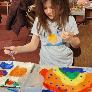 A child is using paint and a brush on a canvas, indicating a guided painting session or an open studio time.