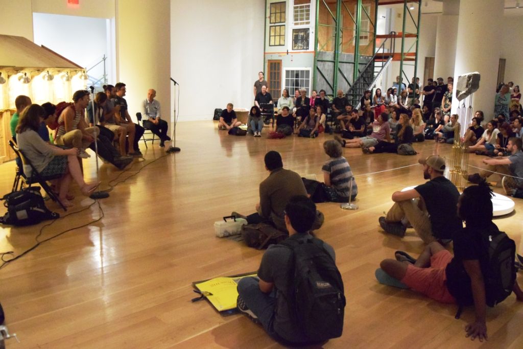 A large group of people sitting on a hardwood floor.