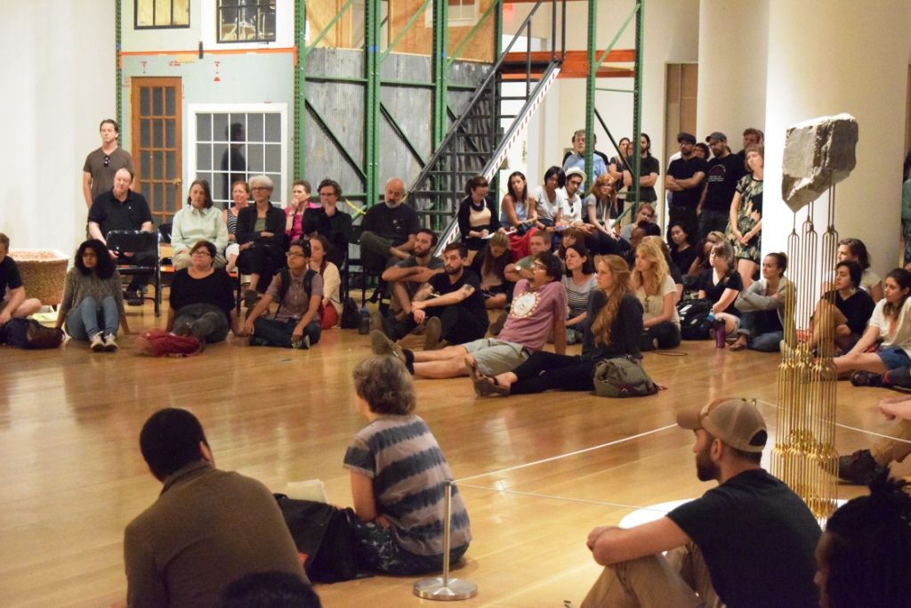 A large group of people sitting on a hardwood floor.