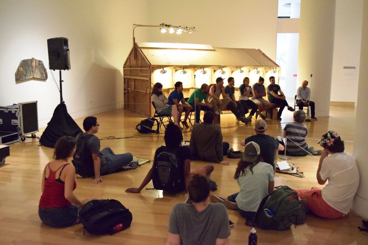 A small group of people sitting on the floor in front of a panel of people in chairs.