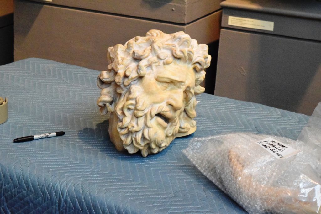 A sculpted head resting on a blue moving pad next to a plastic bag and a marker
