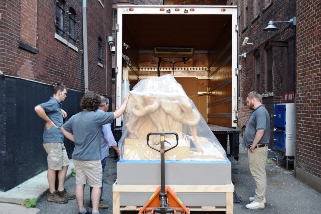 Three people with the artwork wrapped in plastic in front of an open moving truck