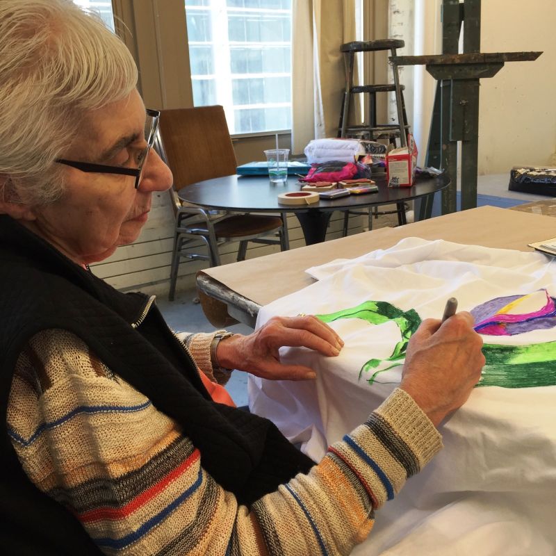 A woman paints a t-shirt at a desk