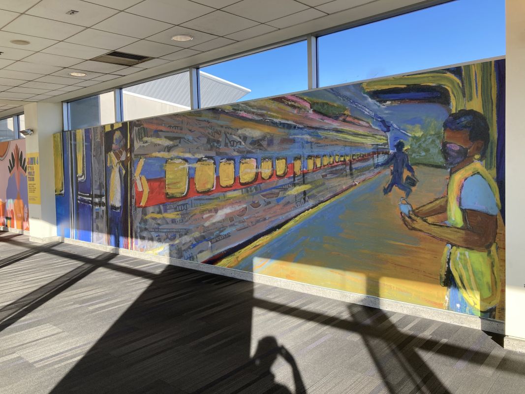 Mural on wall in airport depicts subway stations and riders