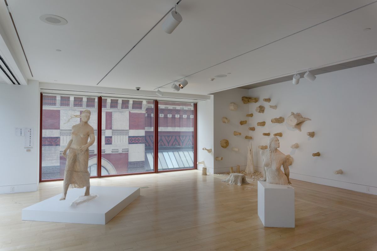 Large gallery space display full figurative sculpture with torso sculpture and casts of tree stumps on the wall