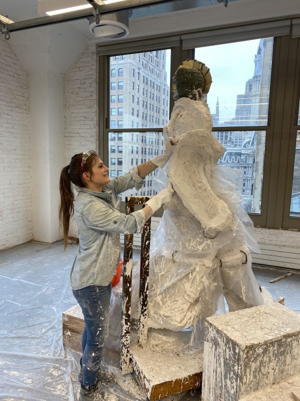 Woman splattered with plaster works on assembling large figurative statue