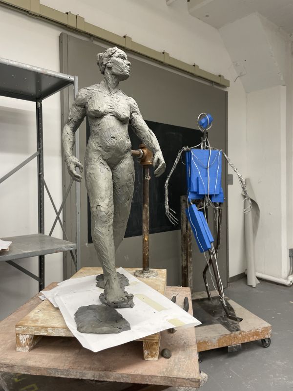 Unfinished sculpture of woman displayed next to wire sculpture of same figure