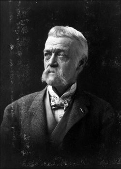 Elderly man with a white mustache and sideburns gazes thoughtfully to the side. Dressed in a suit and bow tie, he exudes an air of wisdom.