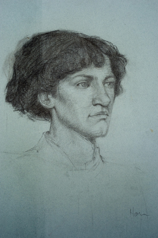 A monochromatic, realistic graphite portrait drawing depicts a light-skinned person with dark, wavy chin-length hair looking toward the right in three-quarter profile against a plain blue-grey background.