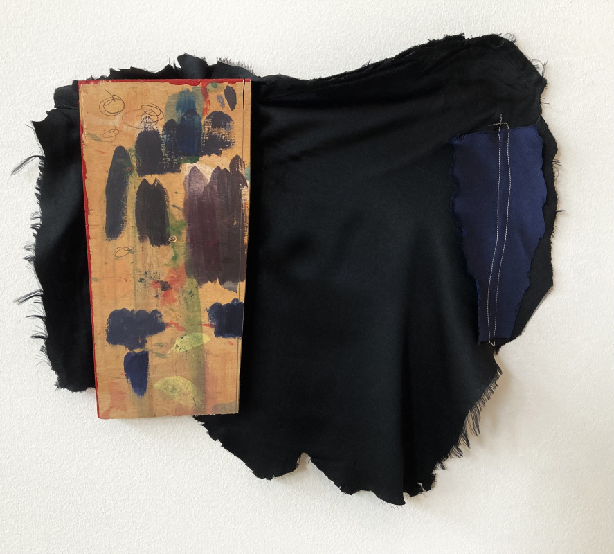 A mixed-media abstract artwork features a painted wooden block mounted on a large piece of frayed black fabric with a stitched blue patch on the side.
